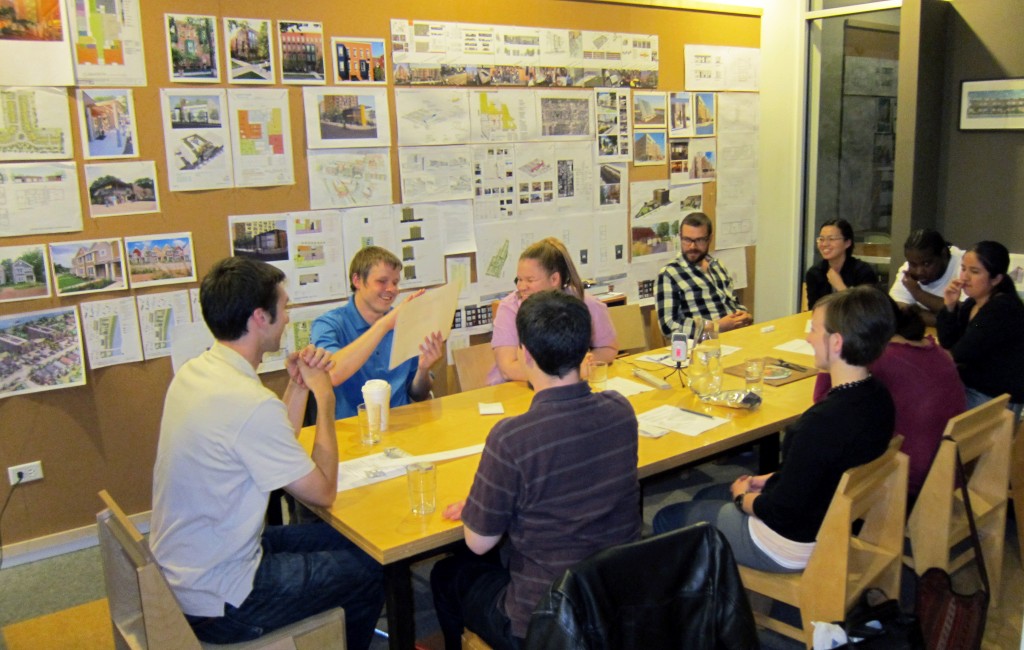 In this image, a focus group of people with low or now vision sit around a long table, talking and providing feedback to the designers about their work to create new tactile graphics.